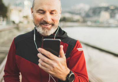 A middle aged man on a beach front pier, looking at his mobile phone 